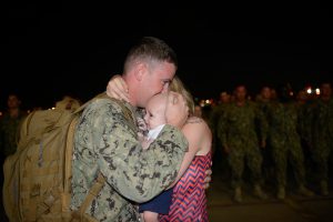 A Port Security Unit 307 member embraces his wife and newborn child after returning home from a nine-month deployment to Guantanamo Bay, Feb. 27, 2017. While deployed, PSU 307 members provided maritime defense of military operations, facilities and personnel in support of Operation Freedom's Sentinel. U.S. Coast Guard photo by Petty Officer 3rd Class Nicole J. Groll.